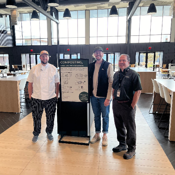 Three people smiling next to composting sign